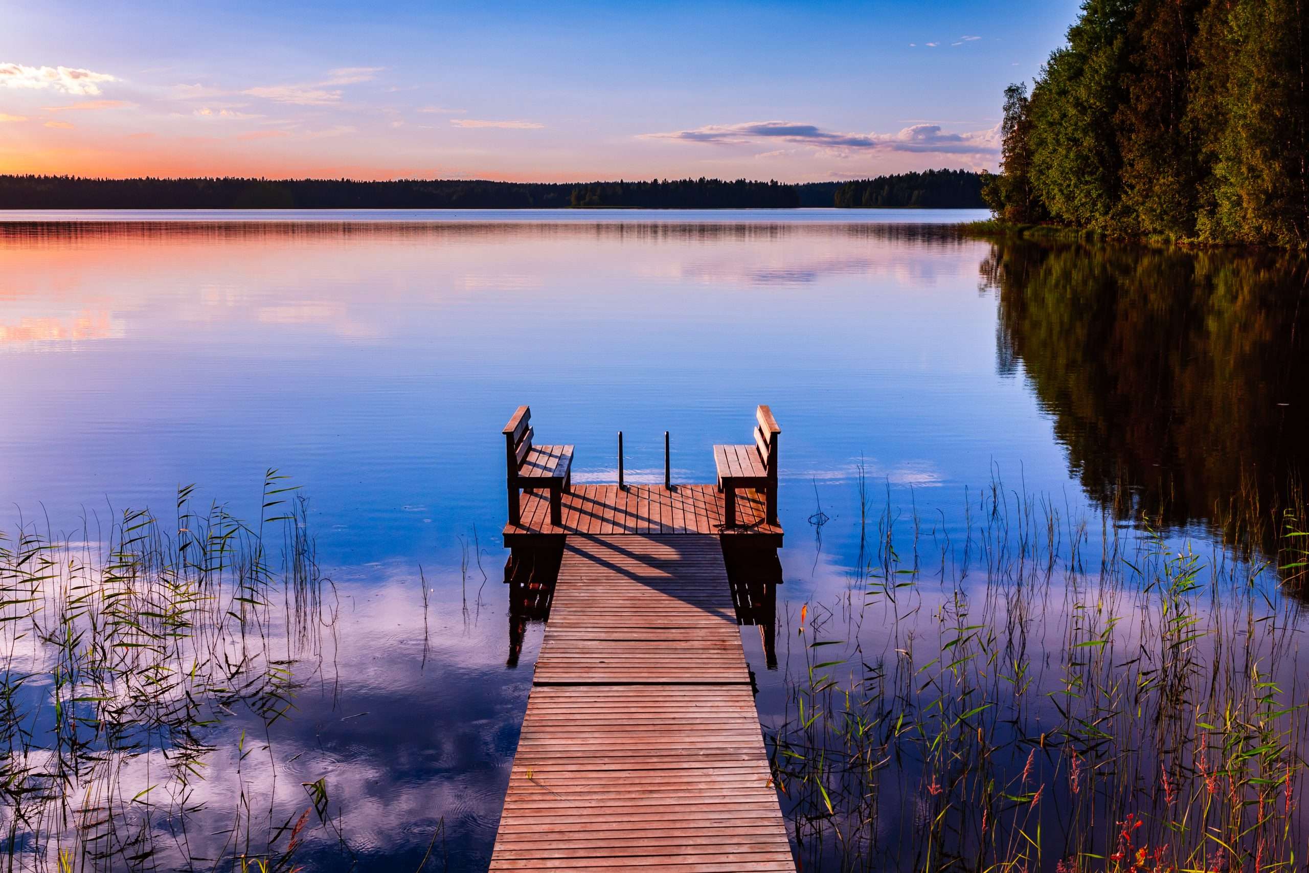 Perspective view of a wooden pier with chairs on the lake at sun